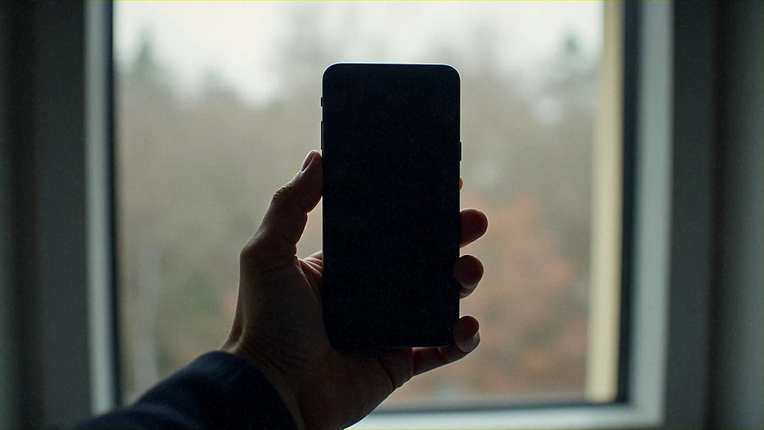 窓辺で画面が消えたスマホを手に持っている様子です。